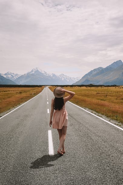Mt-Cook, Mt-Cook-Road, Mt-Cook-Instagram, Best-Instagram-Places-South-Island-Mt-Cook, girl-crossing-road-pink-dress-mountains-snow-yellow-fields
